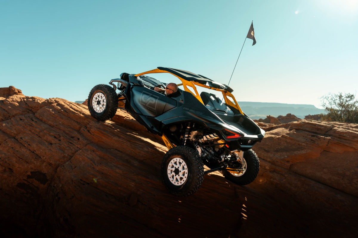 Can-Am Maverick X3 climbing a steep red rock ledge at Sand Hollow State Park near St. George Utah with desert mountains in the background