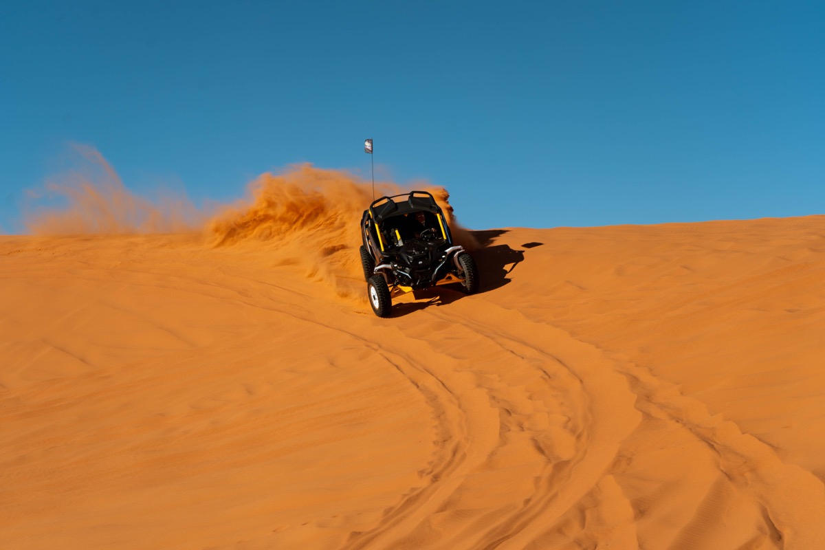 UTV powering up a steep orange sand dune face at Sand Mountain near Delta Utah with blue sky and massive sand roost behind